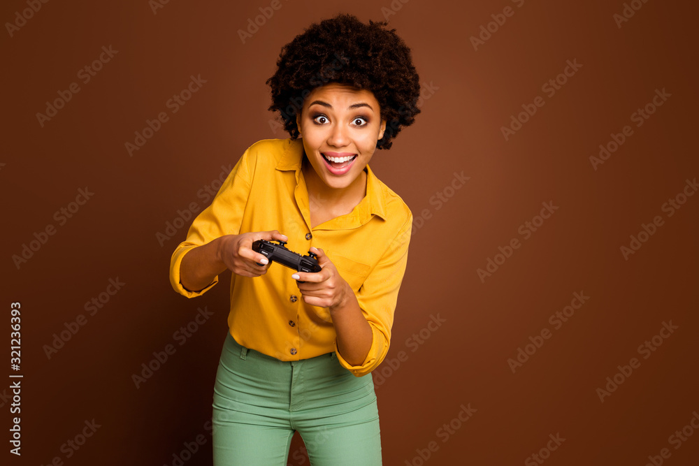 Photo of crazy funny dark skin wavy lady hold joystick plying video game addicted gamer online team leader wear yellow shirt green pants isolated brown color background Photo of crazy funny dark skin wavy lady hold joystick plying video game addicted gamer online team leader wear yellow shirt green pants isolated brown color background