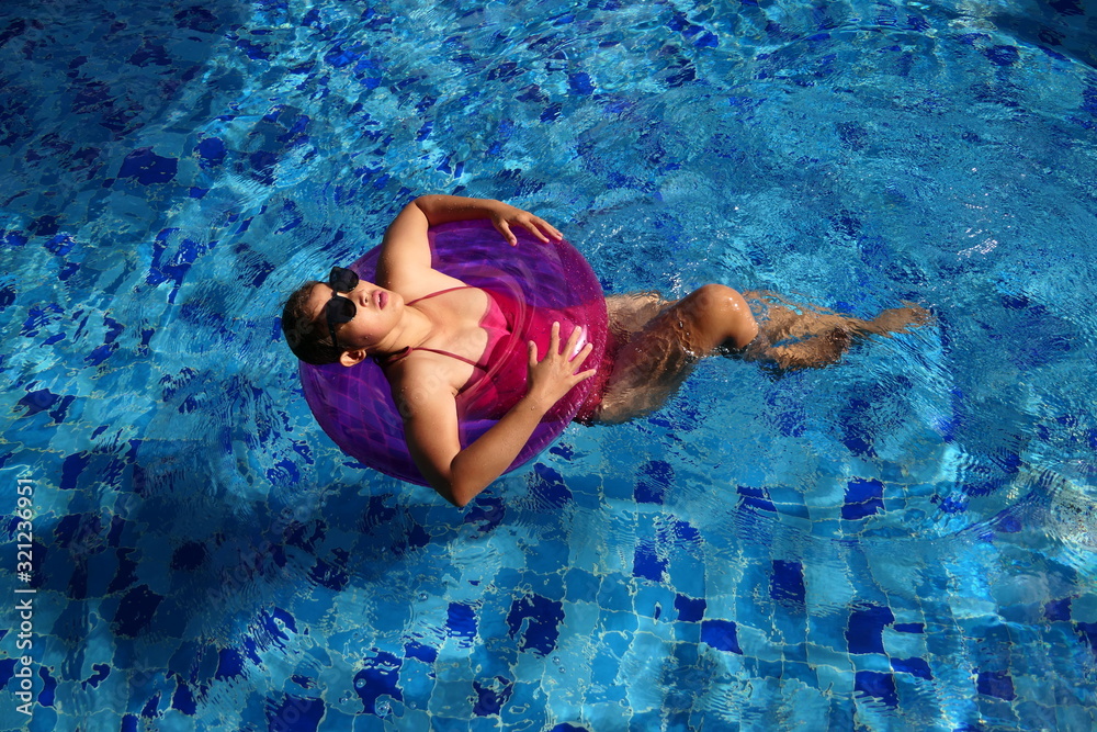 Asian woman wearing red swimsuit and sunglasses relaxing on the inflatable swim ring in the swimming pool. Vacation and holiday concept.