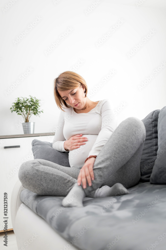 Pregnant tired exhausted woman with stomach, leg and pain issues at home on a couch, being sick.