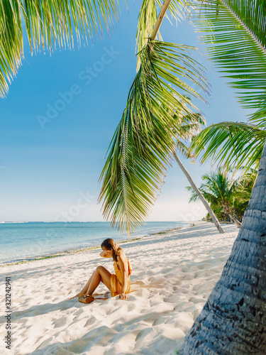 Young woman in dress relaxing at tropical palm beach. Tropical vacation in paradise