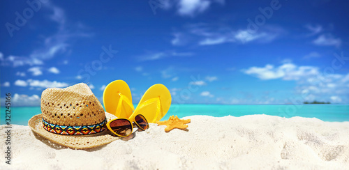 Concept summer beach holiday. Beach accessories - straw hat, glasses, starfish, yellow flip-flops on sandy tropical beach against blue sky with clouds on bright sunny day. Beautiful colorful image. photo