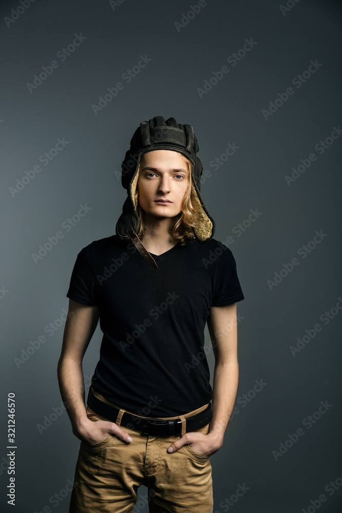 Young guy model posing in a tankman helmet on the gray background. hands in pockets Young guy model posing in a tankman helmet on the gray background. hands in pockets