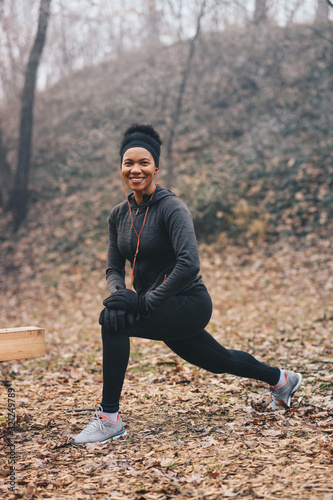 A young woman stretching and looking at the camera outdoors.