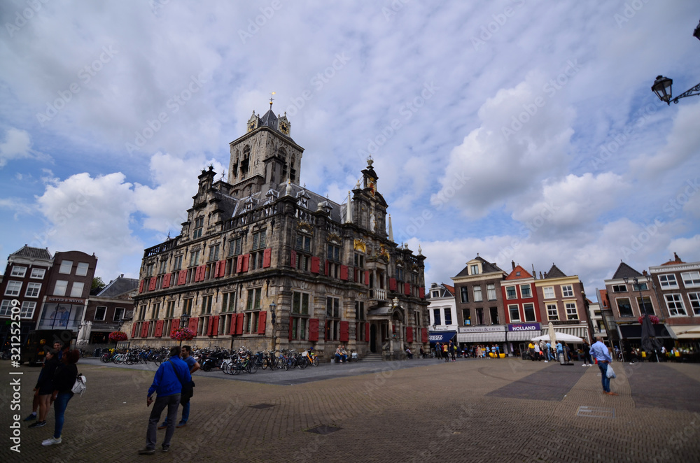 Delft, the netherlands, august 2019. The imposing town hall: on the dark stone facade stand out the red windows and the golden decorations. Blue sky with white clouds.
