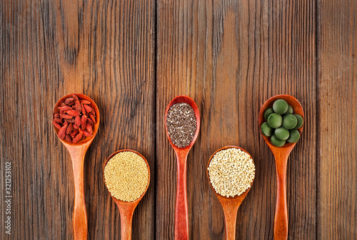 Fototapeta Naklejka Na Ścianę i Meble -  Goji berries, amaranth seeds, chia seeds, quinoa seeds, spirulina tablets in the spoons on a wooden background.