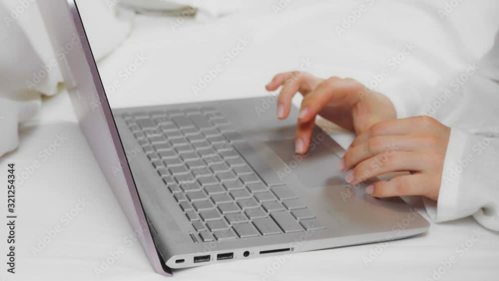 Woman working with her laptop while sitting on a snow-white bed, top view Woman working with her laptop while sitting on a snow-white bed, top view