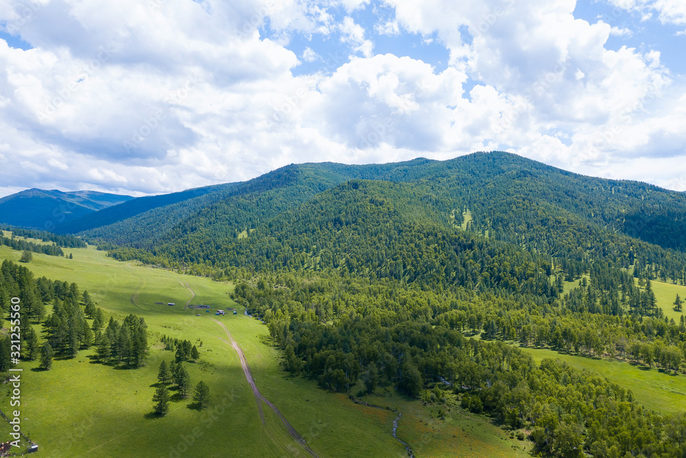 Fototapeta premium Aerial landscape with mountains, green trees, field, road and river under blue sky and clouds in summer