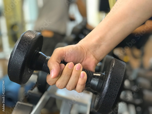 The right man’hand is lifting a dumbbell from the rack. The dumbbell is used for helping to strip away fat as well as building lean muscle.
