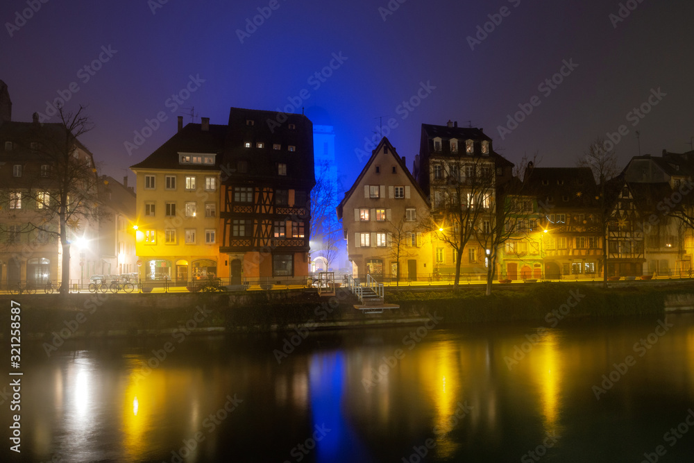 Ile River Embankment in Strasbourg at night, fog. Reflections of illuminated buildings and lanterns in the water