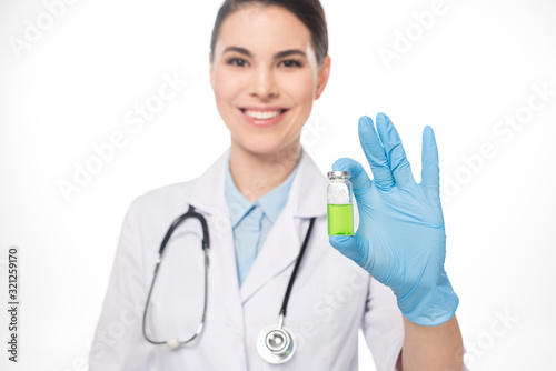 Selective focus of smiling doctor holding jar with green vaccine isolated on white