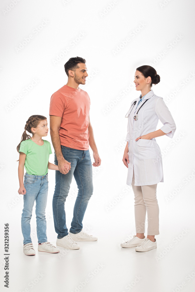 Full length of female pediatrician smiling at father with daughter on white background Full length of female pediatrician smiling at father with daughter on white background