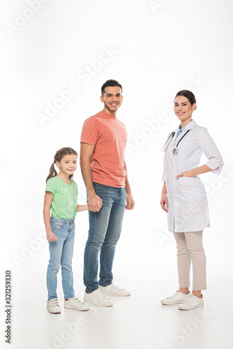 Full length of pediatrician near father with daughter smiling at camera on white background