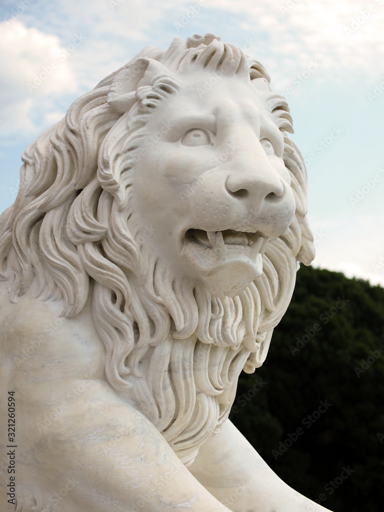 Decorative stone sculpture of a lion on the background of the sky and garden. Fragment of the sculpture, side view. Decorative stone sculpture of a lion on the background of the sky and garden. Fragment of the sculpture, side view.