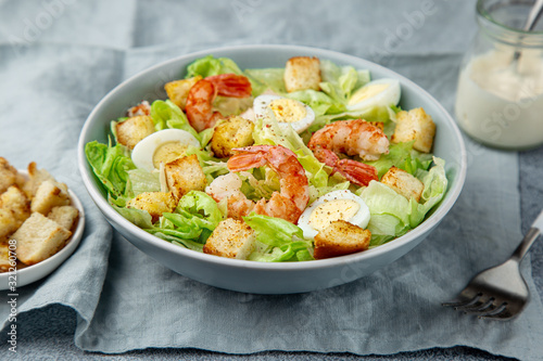 Caesar salad with prawn, roasted chicken, croutons and cheese in blue bowl