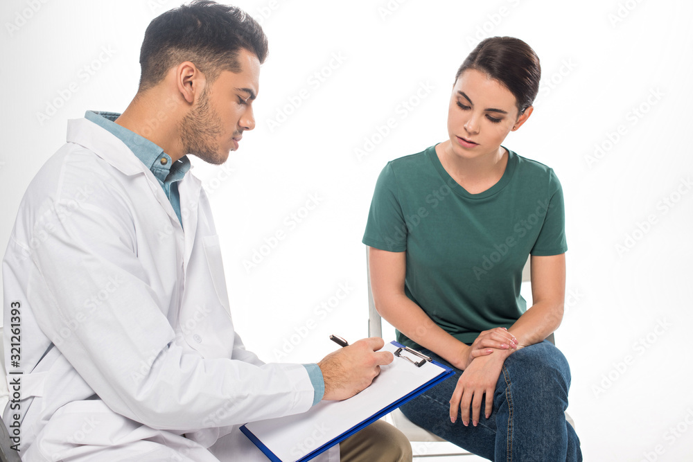 Handsome doctor writing on clipboard near female patient isolated on white Handsome doctor writing on clipboard near female patient isolated on white