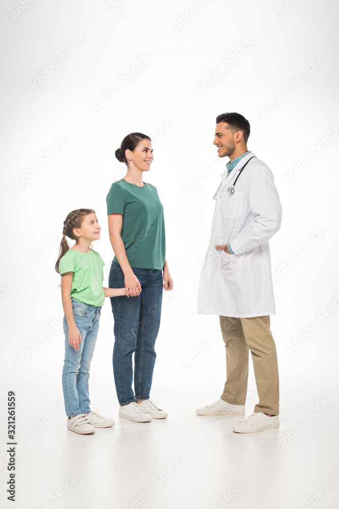 Full length of mother with daughter smiling at pediatrician on white background