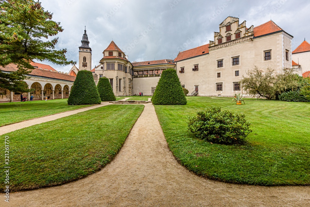 Telc / Czech Republic - September 27 2019: View of a state owned castle and a church of James the Great from a garden with green grass, bushes and sandy footpath.