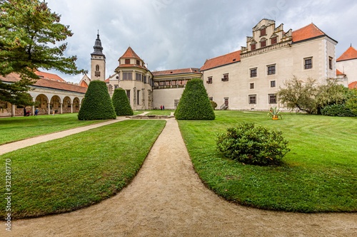 Telc / Czech Republic - September 27 2019: View of a state owned castle and a church of James the Great from a garden with green grass, bushes and sandy footpath.