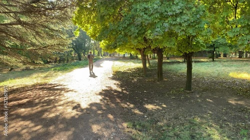 POV walking on footpath in sunny autumn park. Sun shining through tree branches