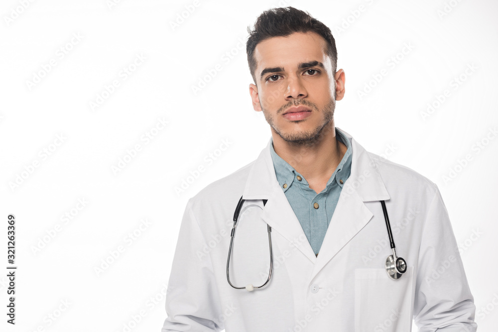 Handsome doctor in white coat looking at camera isolated on white