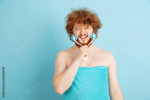 Portrait of young caucasian man in his beauty day and skin care routine. Male model with natural red hair massaging faceskin with stone roller. Body and face care, natural, male beauty concept. photo