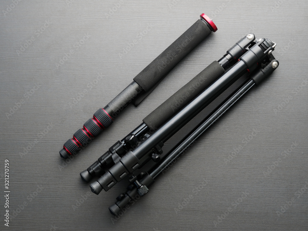 Black modern quality tripod and monopod together on a dark table. Black modern quality tripod and monopod together on a dark table.