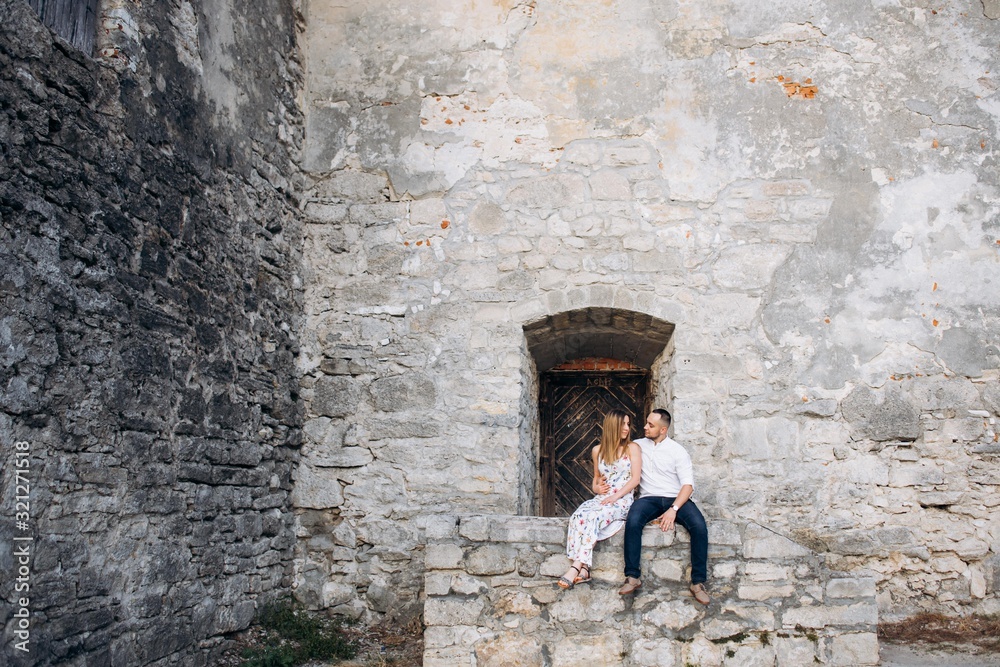 Wonderful couple in love looking to each other and sitting near the stone wall of old castle