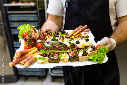Chef or waiter holding platter full of fresh canapes finger food snacks for buffet meal at restaurant.