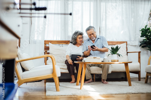 Foto Happy Asian senior couple using smartphone together on couch in living room, old