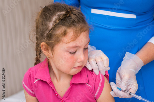 A sad, crying baby watches him being vaccinated in his shoulder. A little girl is very worried about an antiviral injection. The kid is afraid of vaccination. Children's medical concept