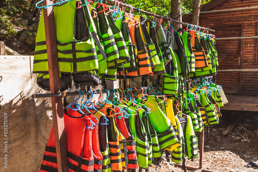 Many colorful life vests of yellow, orange, green and red colors hanging outdoor on sunny summer day. Special equipment for safe canoeing in rocky canyon.