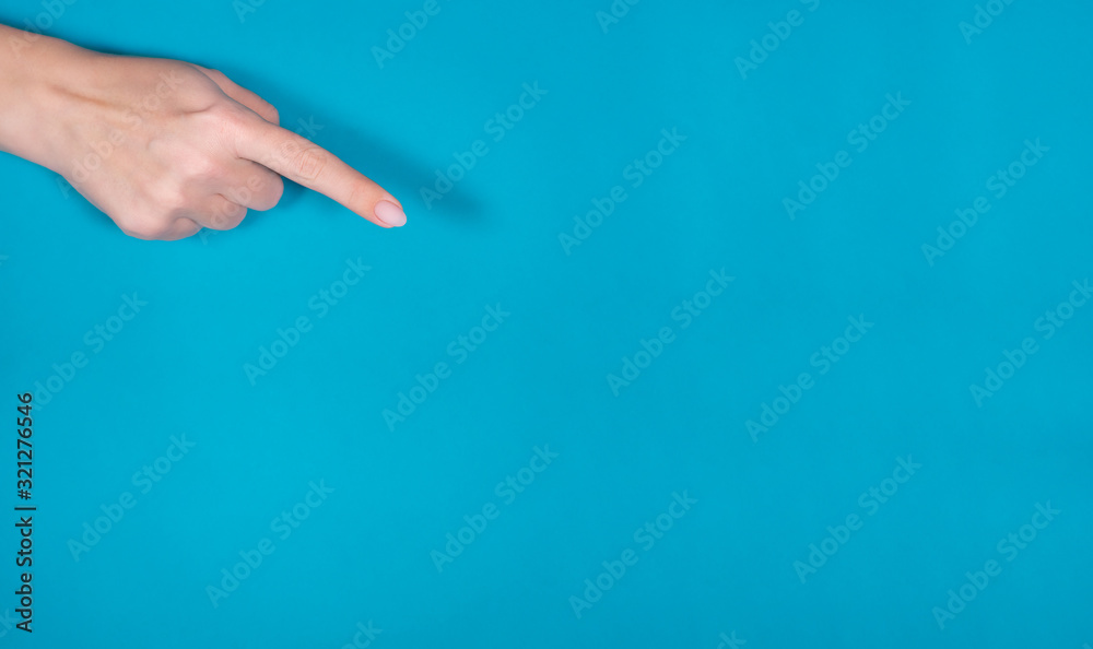 Closeup view of beautiful female hand with pastel nude look manicure isolated on bright blue background with copyspace. Horizontal photography of woman raising one index finger up pointig at something