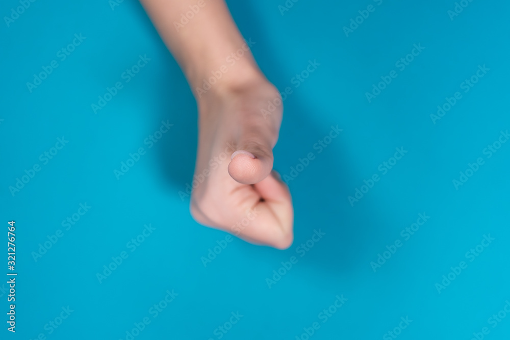 Closeup top view photography of beautiful manicured female hand making like and approval gesture holding big thumb up isolated on bright blue background. Shallow depth of field. 