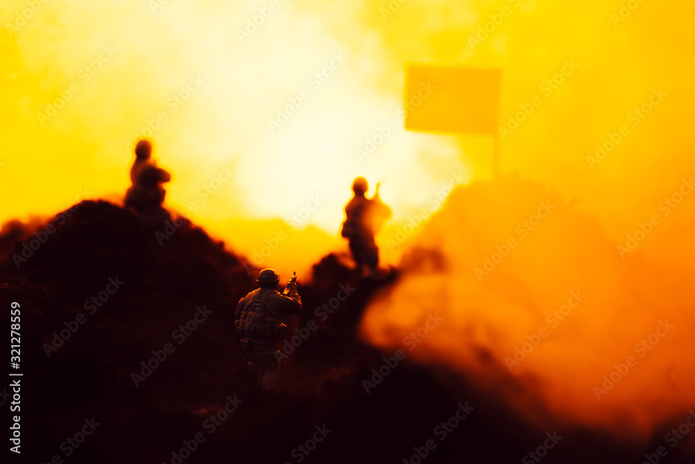 Selective focus of toy warriors on battleground with smoke, flag and fire at background