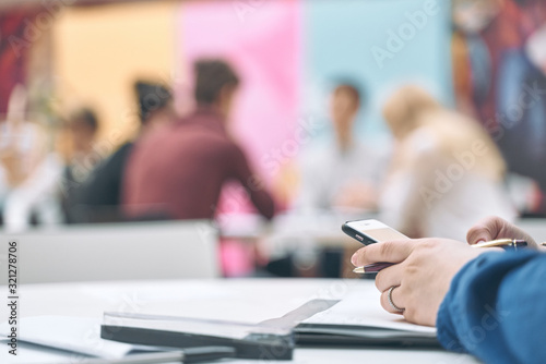 Business person holding modern smartphone and touching on a blank screen. Stylish modern office workplace on a background.