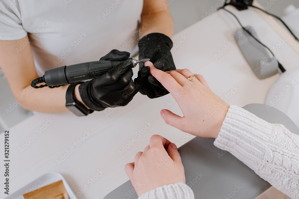 Woman use electric nail file drill in beauty salon. Nails manicure process in detail