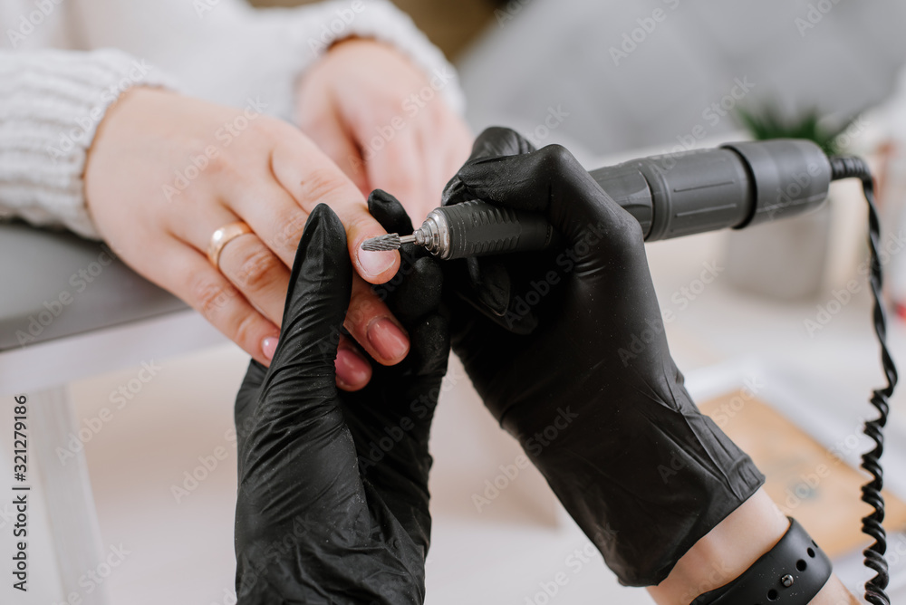 Woman use electric nail file drill in beauty salon. Nails manicure process in detail
