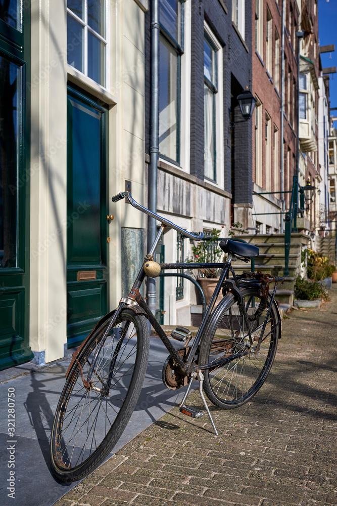 A rusty bicycle parked outside on a cobblestone sidewalk in an iconic neighborhood of Amsterdam
