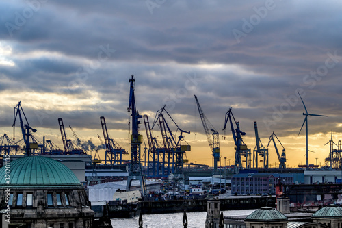 Der Hamburger Hafen am Abend mit Hafenkränen und Windrädern im Gegenlicht