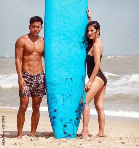 Young handsome man and beautiful woman wearing black swimming suit posing beside serf board on the beach,with enjoy and happy feeling