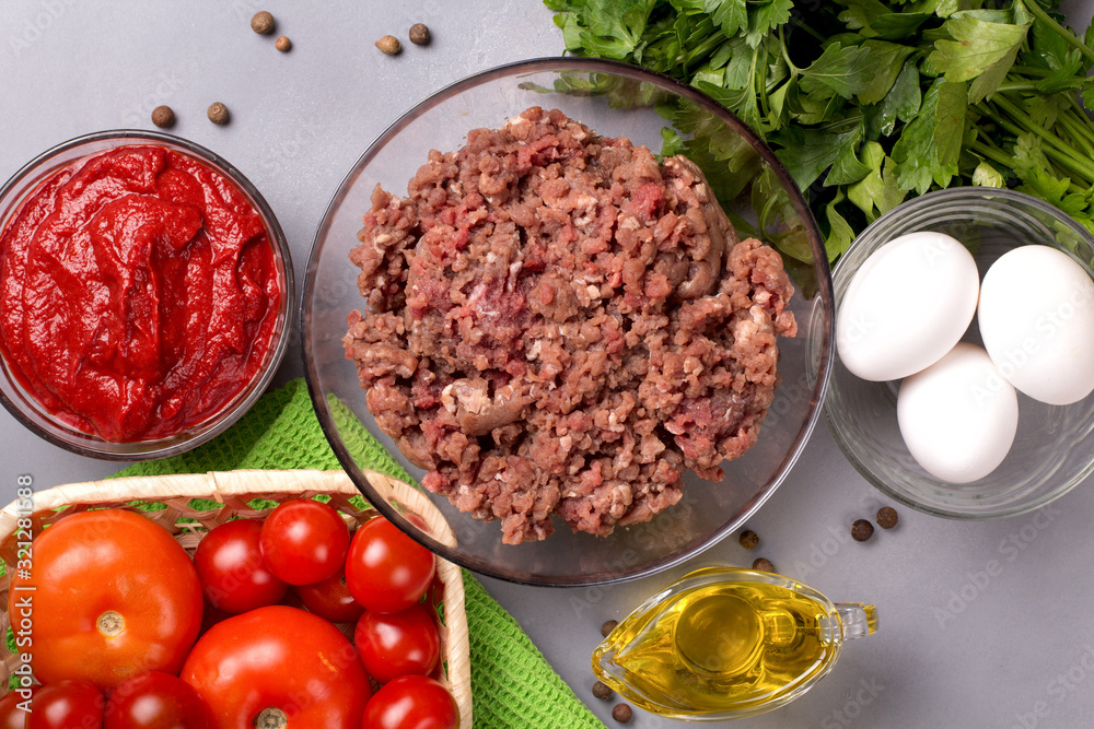 Minced meat with tomatoes, eggs, parsley and pepper on a gray background. Forcemeat. Top view. Minced meat with tomatoes, eggs, parsley and pepper on a gray background. Forcemeat. Top view.