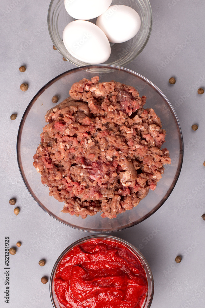 Minced meat with tomatoes, eggs, parsley and pepper on a gray background. Forcemeat. Top view. Minced meat with tomatoes, eggs, parsley and pepper on a gray background. Forcemeat. Top view.