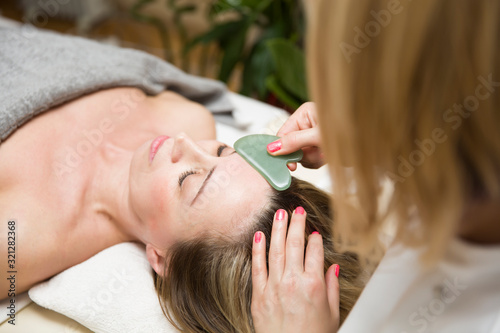 Woman having an gua sha facial massage with natural jade stone massager photo