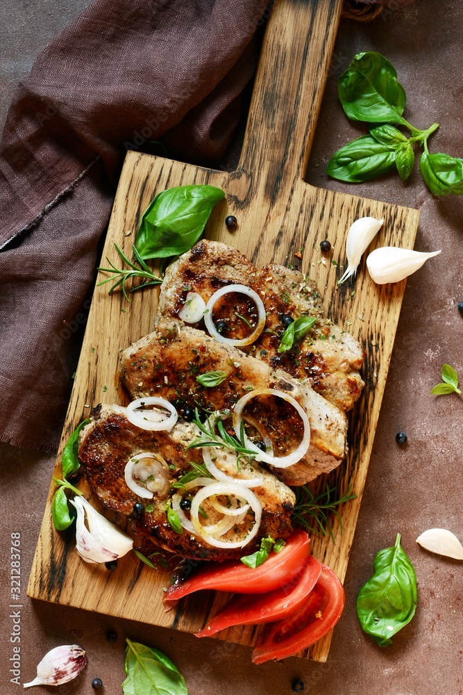 Fried steak with herbs and spices on wooden board with tomato, garlic, onion rings, rosemary and fresh basil leaves Fried steak with herbs and spices on wooden board with tomato, garlic, onion rings, rosemary and fresh basil leaves