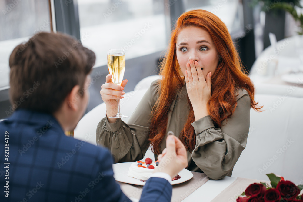 romantic date of lovely caucasian couple in rich restaurant, redhaired lady stay in shock after marriage proposal boyfrined in tuxedo, hold golden ring in hands. love, couple, marriage, anniversary romantic date of lovely caucasian couple in rich restaurant, redhaired lady stay in shock after marriage proposal boyfrined in tuxedo, hold golden ring in hands. love, couple, marriage, anniversary