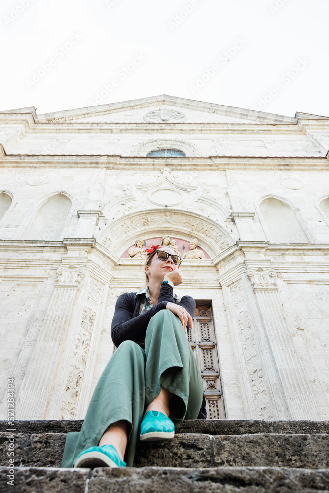 Young female traveler sitting on church steps in old town in Tuscany, Italy
