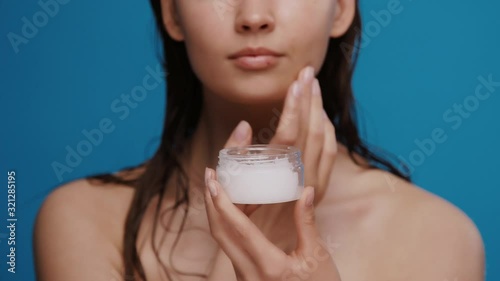 fresh woman after shower moisturizing face with white cream