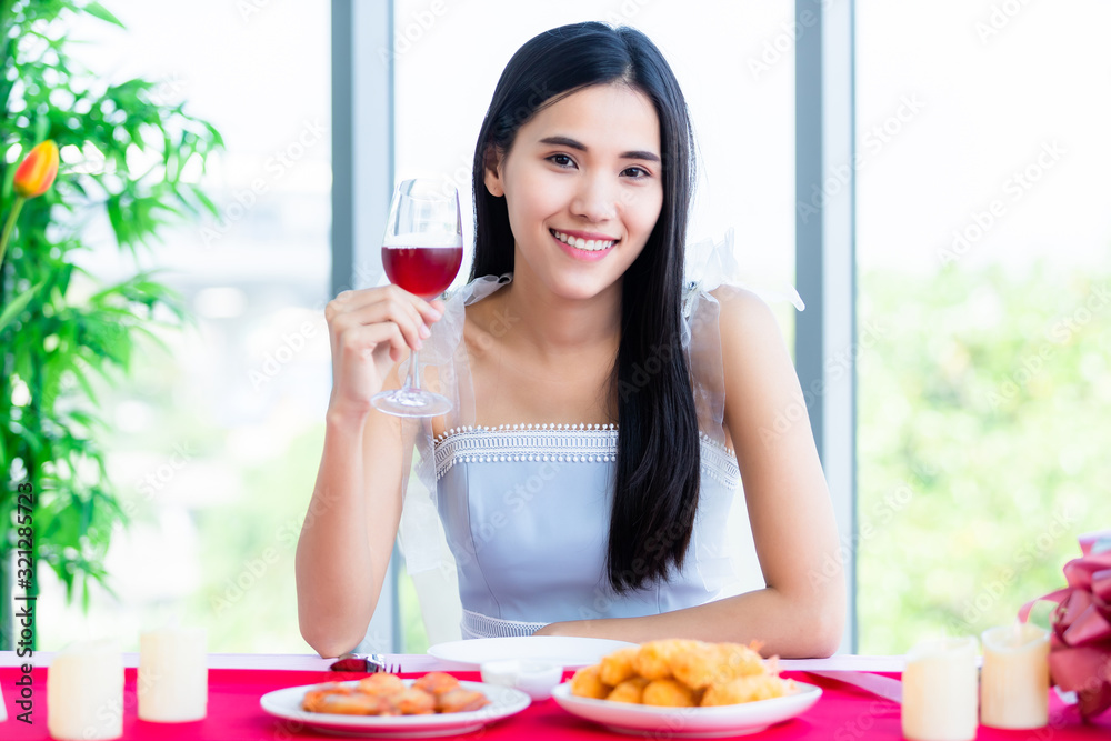 Valentine's day concept, Happy of smiling Asian young female sitting at a table food show holding with wine glasses at in the restaurant background Valentine's day concept, Happy of smiling Asian young female sitting at a table food show holding with wine glasses at in the restaurant background
