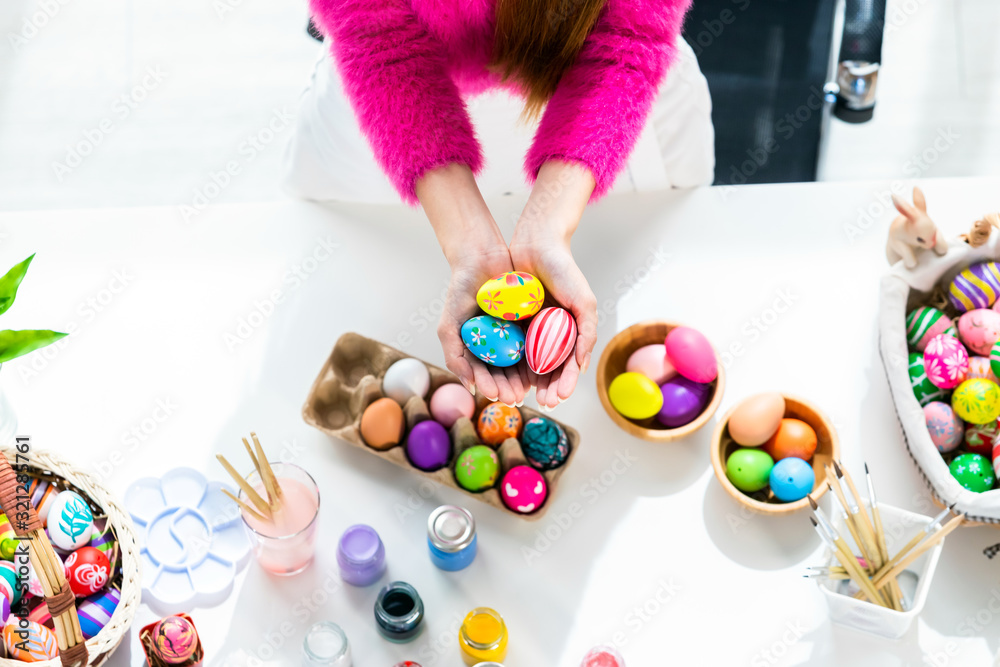 Easter holiday concept,Close up of Happy Asian Young woman holding with colorful Easter eggs on white wooden table background in top view