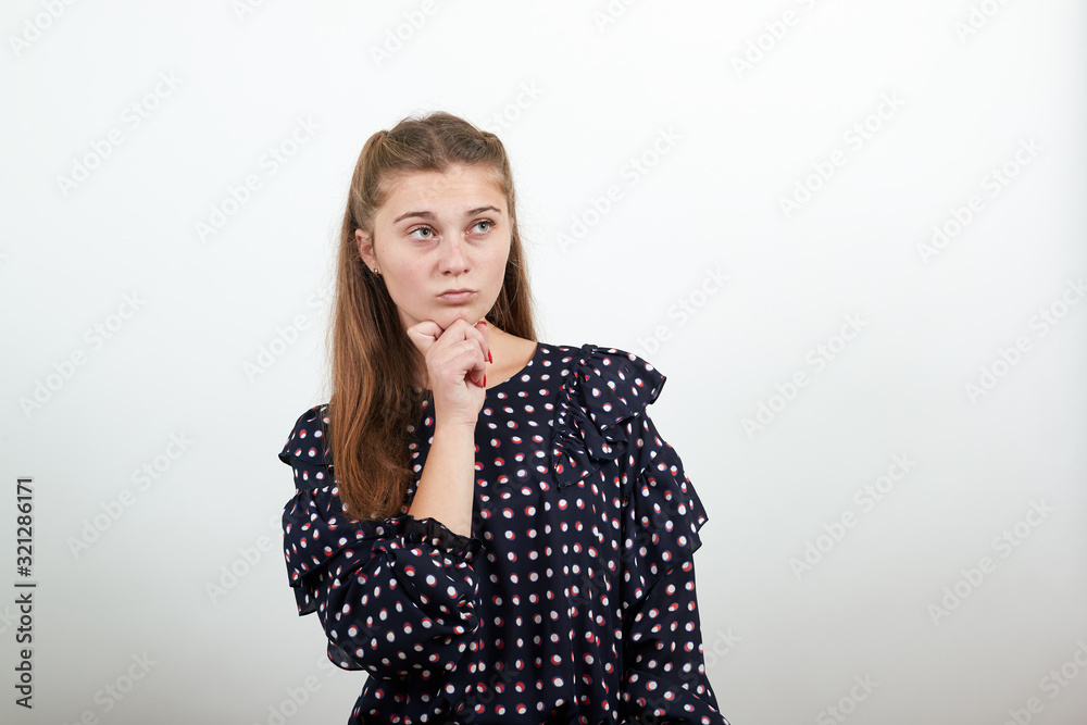Fair-haired beautiful girl in a black dress with white circles thinks makes decision holding her chin with her hand